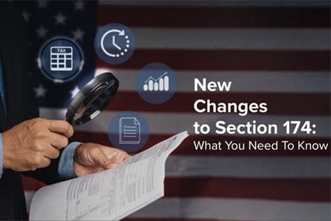 Businessman with magnifying glass reviewing tax forms with the text “New Changes to Section 174: What You Need to Know” on U.S. flag background